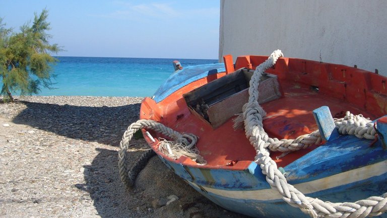 Blau-rotes Fischerboot an Land mit Blick auf das blaue Meer